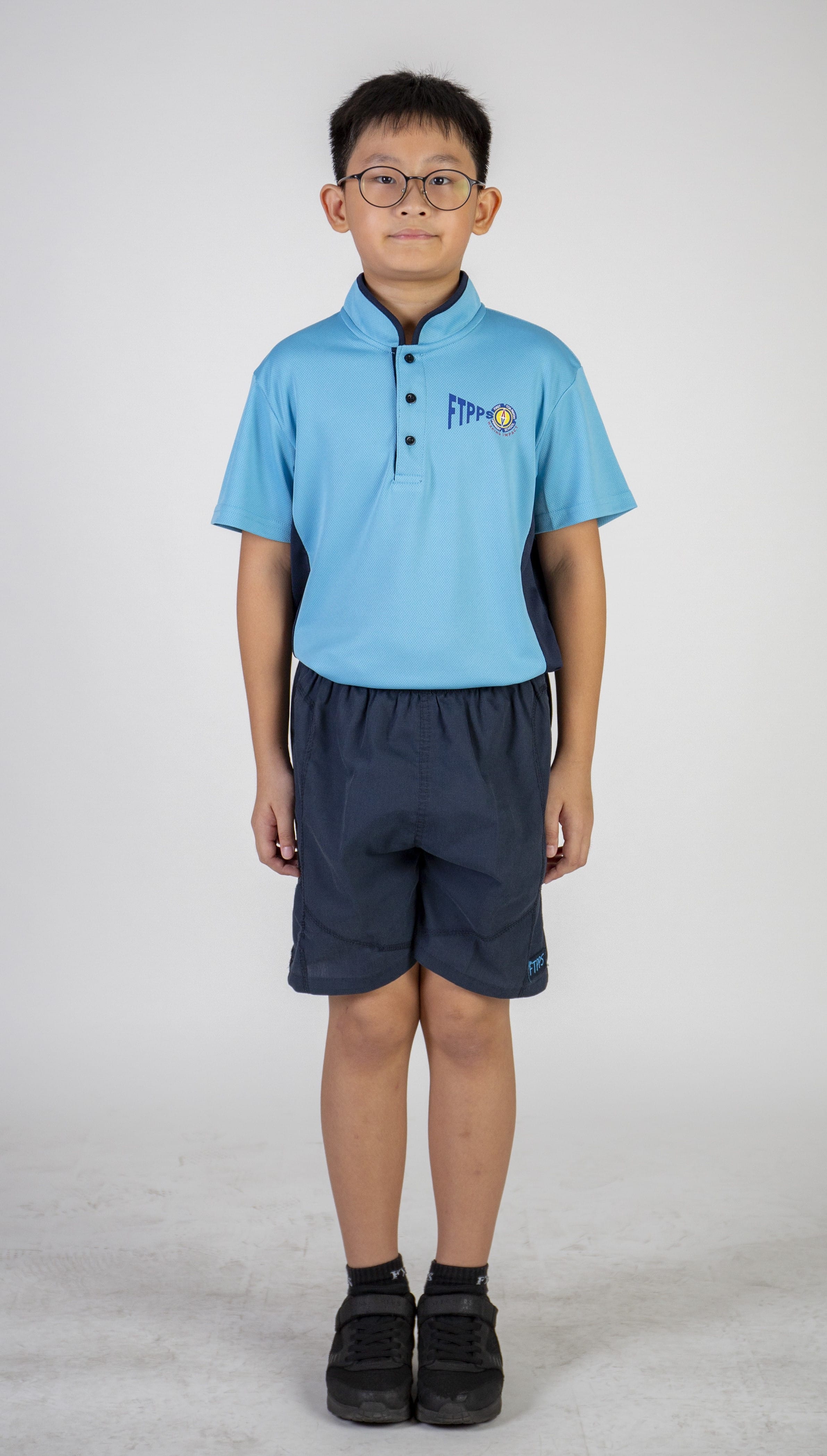Front view of a student wearing a light blue sports polo shirt, navy shorts, black socks, black shoes and round glasses.